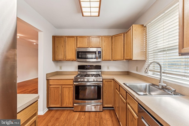 kitchen featuring stainless steel appliances, light countertops, a sink, light wood-type flooring, and baseboards