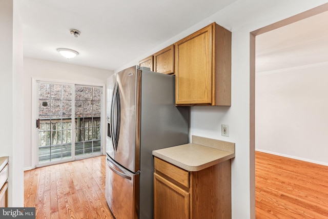 kitchen with stainless steel refrigerator with ice dispenser, light countertops, brown cabinetry, light wood-style floors, and baseboards