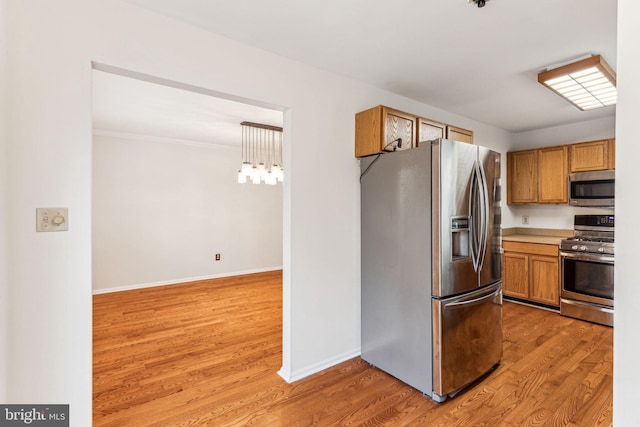 kitchen with light wood-style flooring, brown cabinets, decorative light fixtures, stainless steel appliances, and light countertops