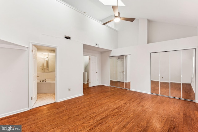 unfurnished bedroom with wood finished floors, visible vents, baseboards, vaulted ceiling, and two closets