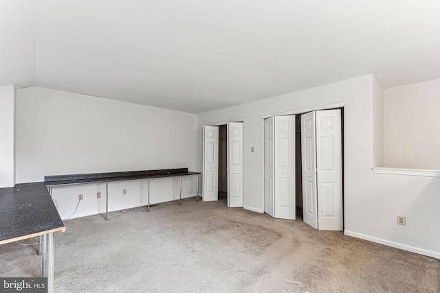 unfurnished bedroom with baseboards, vaulted ceiling, multiple closets, and light colored carpet