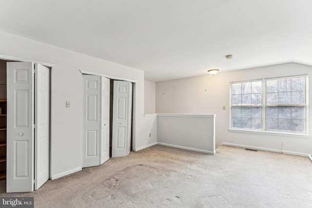 empty room with baseboards, visible vents, vaulted ceiling, and light colored carpet