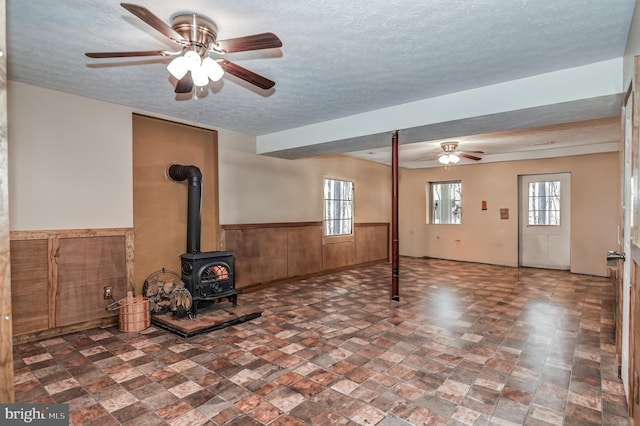 unfurnished living room featuring a textured ceiling, a wood stove, and ceiling fan