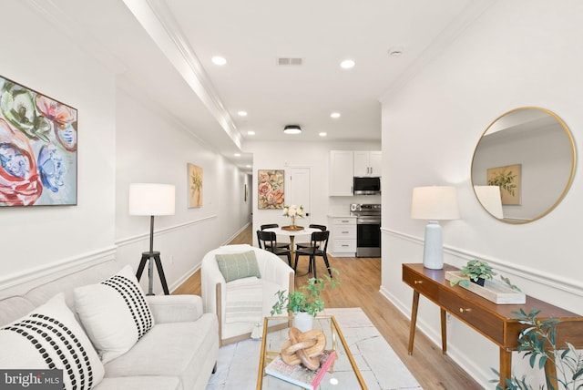 living area with visible vents, baseboards, ornamental molding, light wood-style floors, and recessed lighting