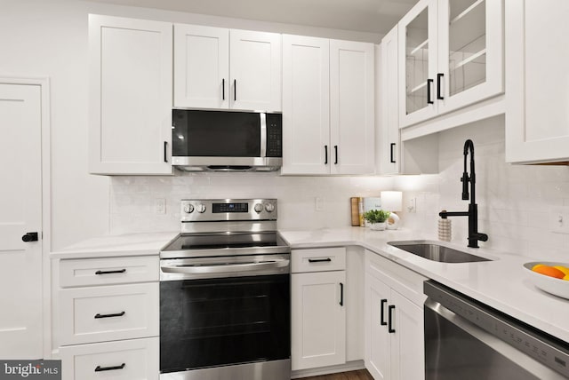 kitchen with a sink, white cabinets, appliances with stainless steel finishes, tasteful backsplash, and glass insert cabinets