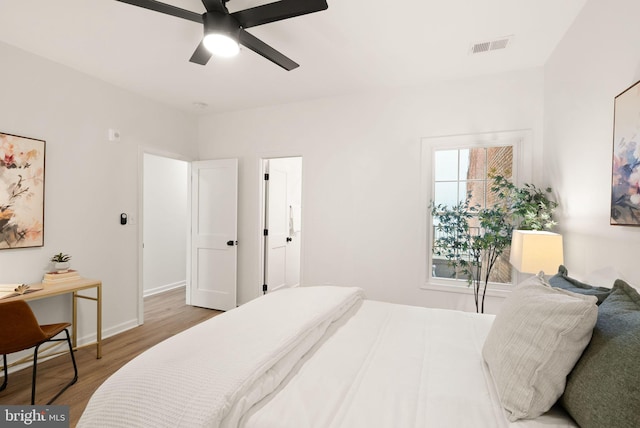 bedroom with a ceiling fan, visible vents, baseboards, and wood finished floors