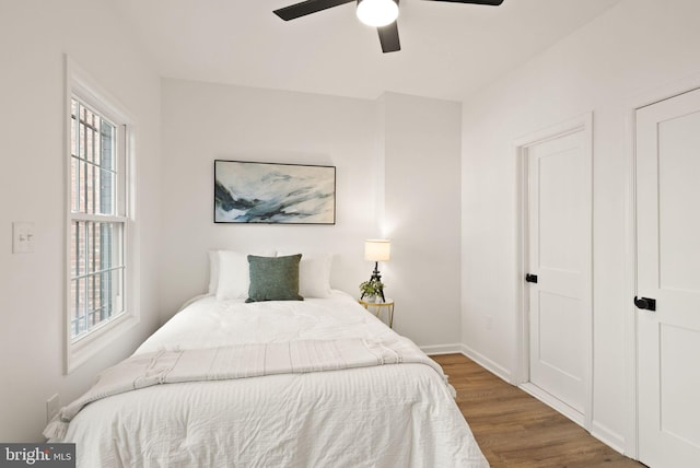 bedroom featuring a ceiling fan, multiple windows, baseboards, and wood finished floors