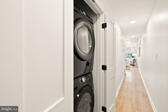 clothes washing area featuring light wood-style flooring, recessed lighting, laundry area, baseboards, and stacked washing maching and dryer