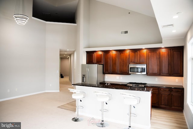 kitchen with hanging light fixtures, stainless steel appliances, a towering ceiling, a kitchen island, and a kitchen bar