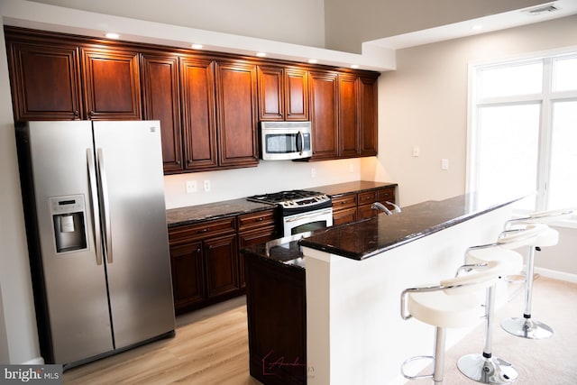 kitchen featuring light wood-type flooring, a breakfast bar, a center island, dark stone counters, and appliances with stainless steel finishes