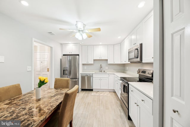 kitchen with light countertops, appliances with stainless steel finishes, white cabinetry, a sink, and light wood-type flooring