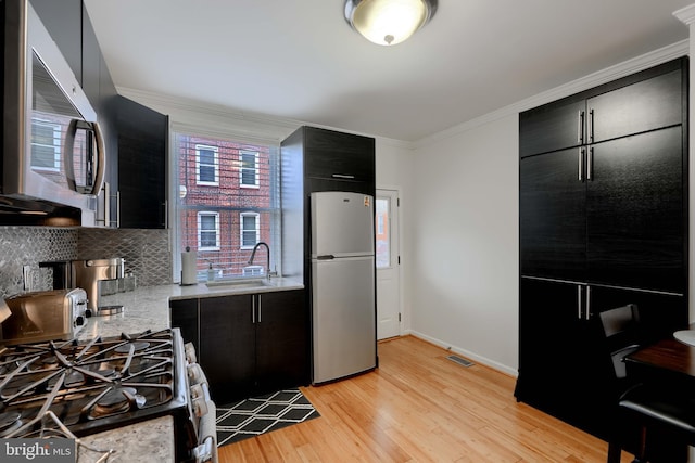 kitchen featuring stainless steel appliances, light countertops, light wood-style floors, a sink, and dark cabinetry