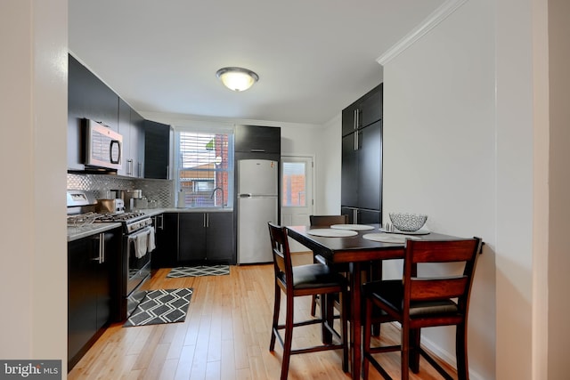 kitchen featuring light wood finished floors, stainless steel appliances, light countertops, decorative backsplash, and dark cabinets