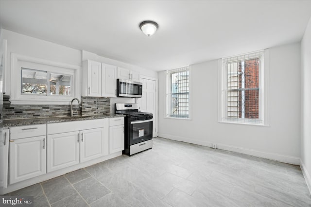 kitchen featuring appliances with stainless steel finishes, sink, dark stone counters, white cabinets, and decorative backsplash