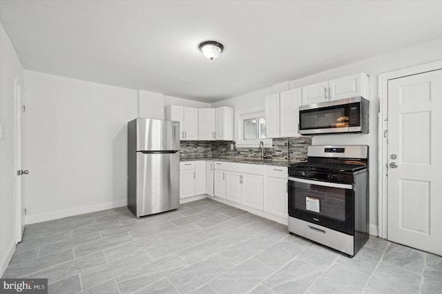 kitchen featuring stainless steel appliances, dark stone counters, white cabinets, decorative backsplash, and sink