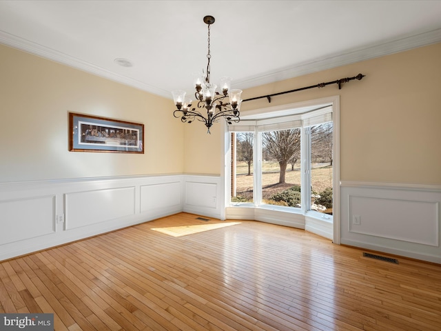 unfurnished dining area with light wood-style flooring, a notable chandelier, a wainscoted wall, visible vents, and crown molding