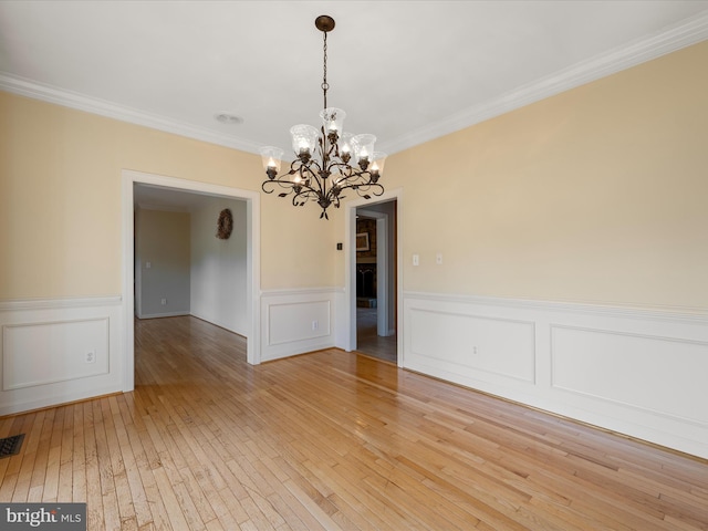 interior space with a wainscoted wall, a notable chandelier, crown molding, and light wood-style flooring