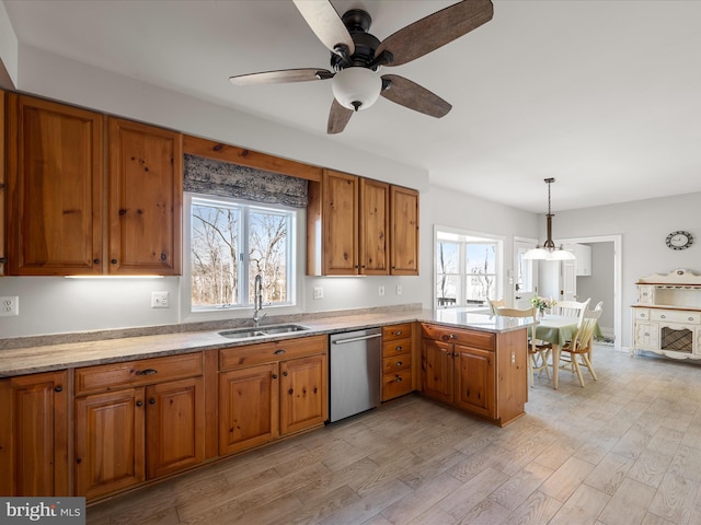 kitchen with a peninsula, a sink, light countertops, stainless steel dishwasher, and decorative light fixtures