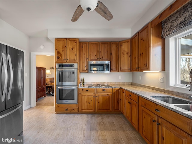 kitchen featuring light stone counters, brown cabinets, light wood-style flooring, a sink, and black appliances