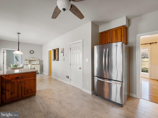 kitchen with freestanding refrigerator, pendant lighting, brown cabinets, and light wood finished floors