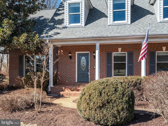 view of exterior entry with brick siding and a shingled roof