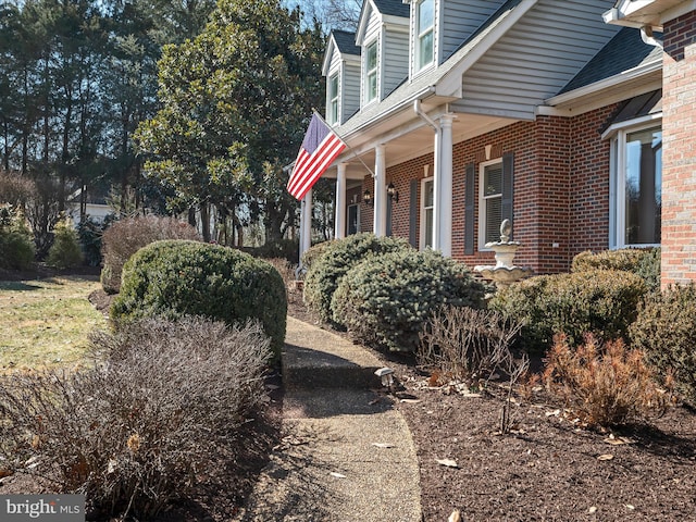 view of home's exterior featuring a porch, brick siding, and roof with shingles