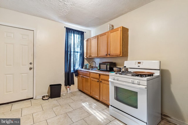 kitchen featuring white range with gas stovetop, light tile patterned floors, sink, and a textured ceiling