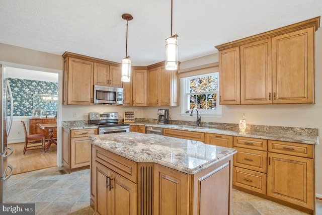 kitchen with stainless steel appliances, a kitchen island, a sink, hanging light fixtures, and light stone countertops