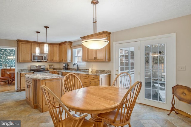 kitchen with a kitchen island, appliances with stainless steel finishes, light stone counters, hanging light fixtures, and a sink