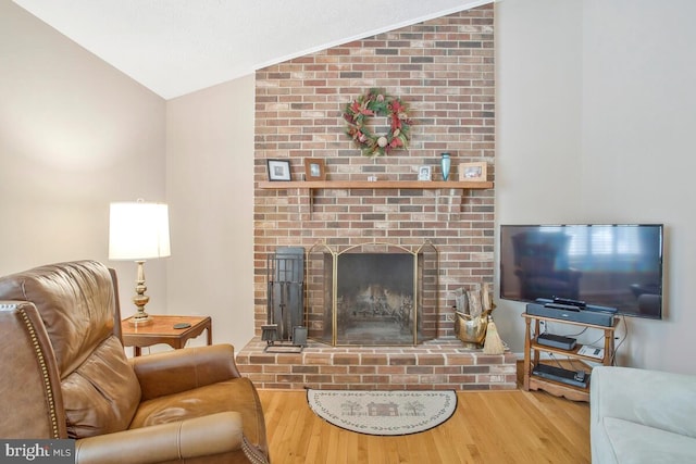 living area with lofted ceiling, a brick fireplace, and wood finished floors