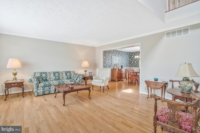 living room featuring baseboards, visible vents, crown molding, and light wood finished floors