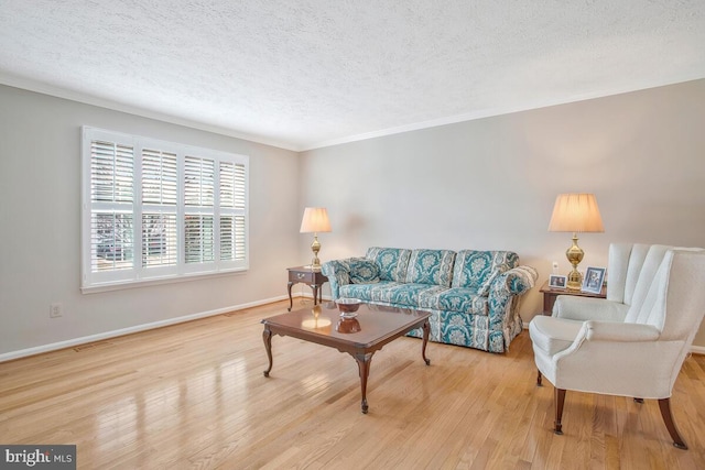 living room with a textured ceiling, crown molding, light wood-style flooring, and baseboards