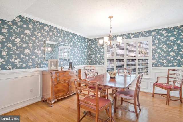 dining space featuring wallpapered walls, a wainscoted wall, light wood-style flooring, a textured ceiling, and a chandelier