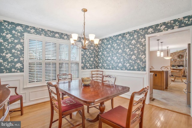 dining room featuring wallpapered walls, wainscoting, an inviting chandelier, a textured ceiling, and light wood-type flooring