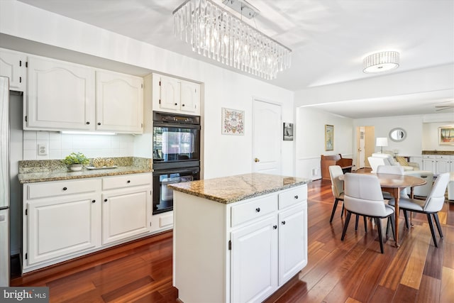 kitchen with light stone countertops, dobule oven black, dark wood finished floors, and decorative backsplash