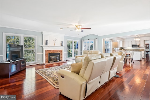 living area with crown molding, a fireplace, lofted ceiling, dark wood-type flooring, and ceiling fan