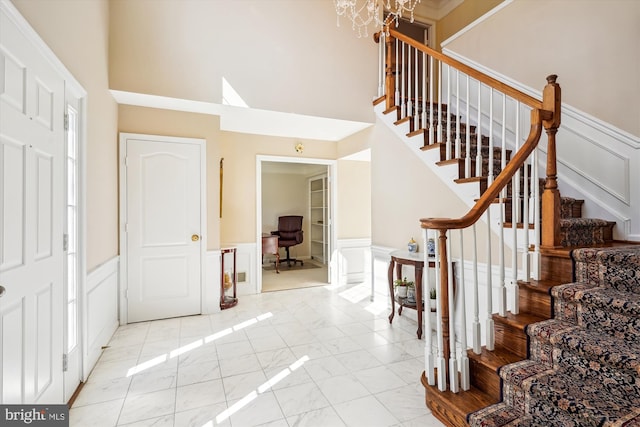 foyer entrance with marble finish floor, wainscoting, a decorative wall, and a high ceiling