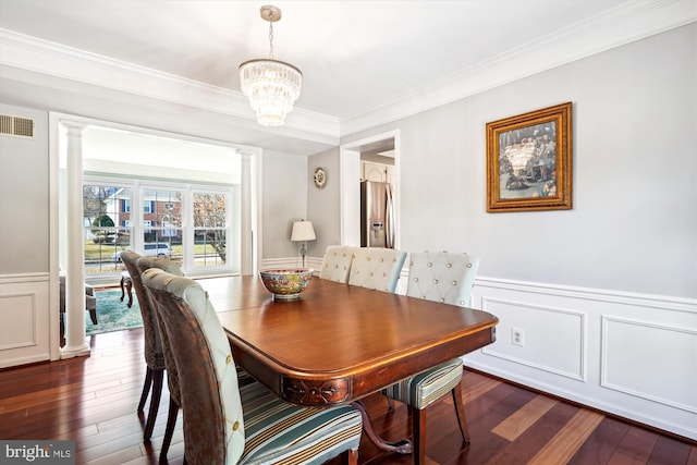 dining area featuring ornate columns, ornamental molding, dark wood-style flooring, and wainscoting