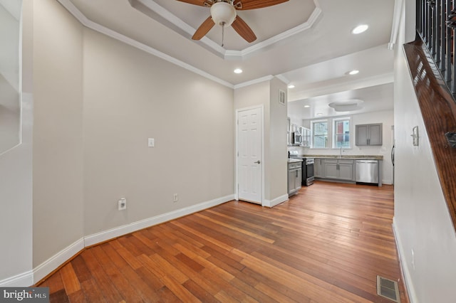 unfurnished living room with crown molding, a raised ceiling, visible vents, baseboards, and hardwood / wood-style flooring