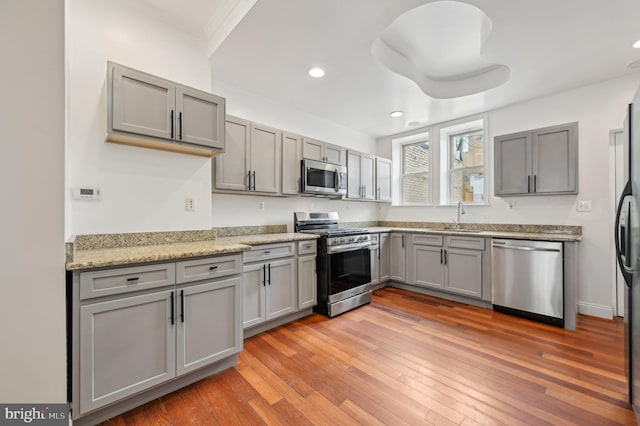 kitchen with stainless steel appliances, light wood-type flooring, gray cabinets, and a sink