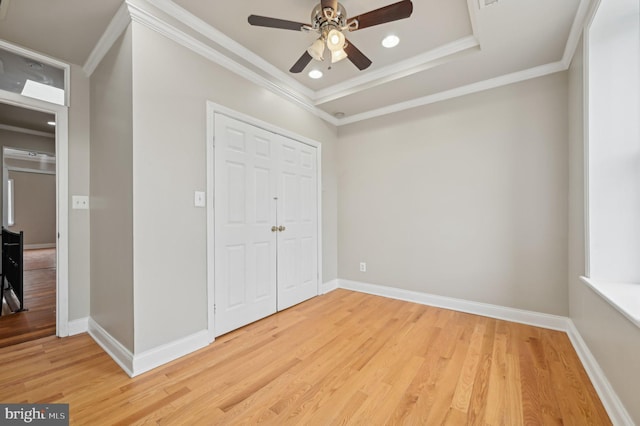 unfurnished bedroom with ornamental molding, a raised ceiling, light wood-style floors, and baseboards