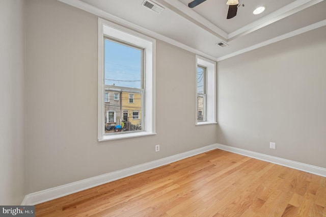 spare room with visible vents, baseboards, ornamental molding, light wood-type flooring, and a tray ceiling