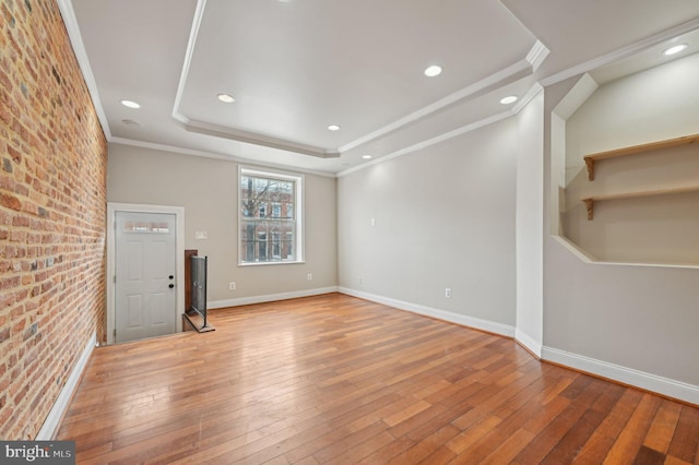 spare room featuring hardwood / wood-style flooring, brick wall, baseboards, ornamental molding, and a raised ceiling