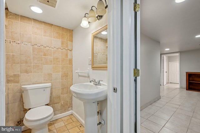 bathroom featuring baseboards, visible vents, toilet, tile patterned floors, and tile walls