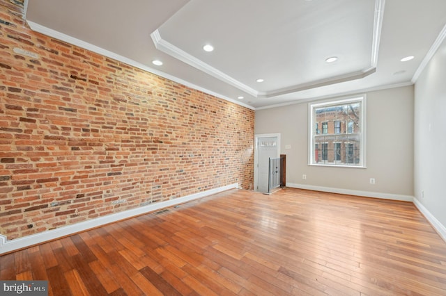 unfurnished room with light wood-style flooring, brick wall, baseboards, ornamental molding, and a raised ceiling