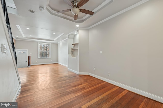 empty room featuring light wood-type flooring, baseboards, a tray ceiling, and ornamental molding