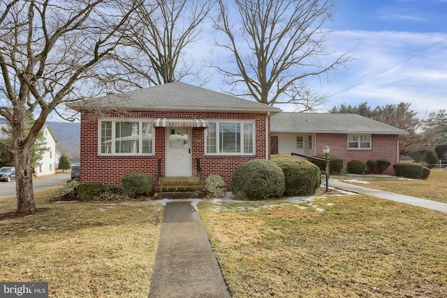 bungalow featuring brick siding, a shingled roof, and a front yard