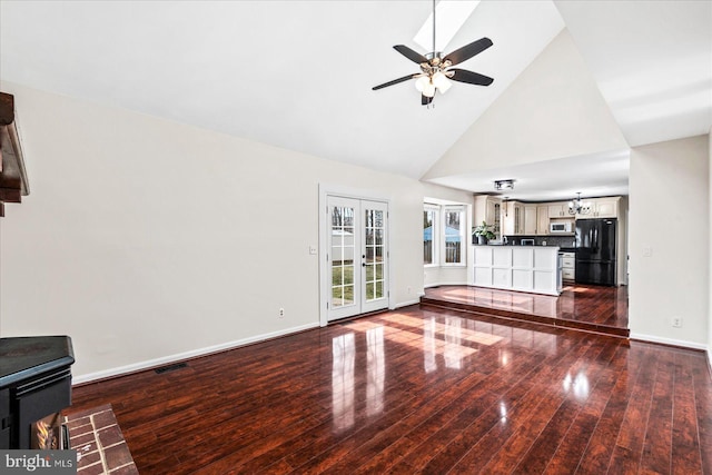 unfurnished living room featuring ceiling fan with notable chandelier, high vaulted ceiling, wood-type flooring, and french doors