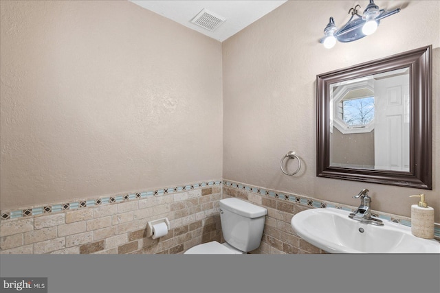 bathroom with sink, toilet, and tile walls