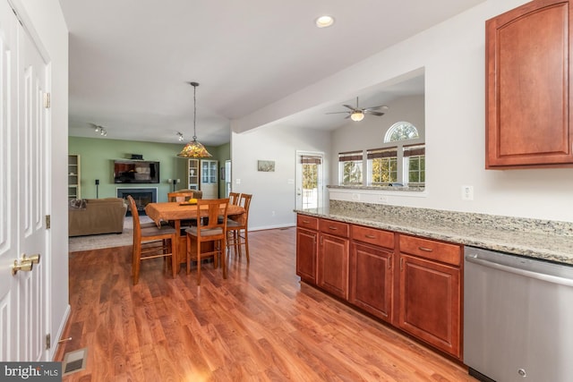 kitchen featuring vaulted ceiling, light stone counters, pendant lighting, light hardwood / wood-style floors, and stainless steel dishwasher